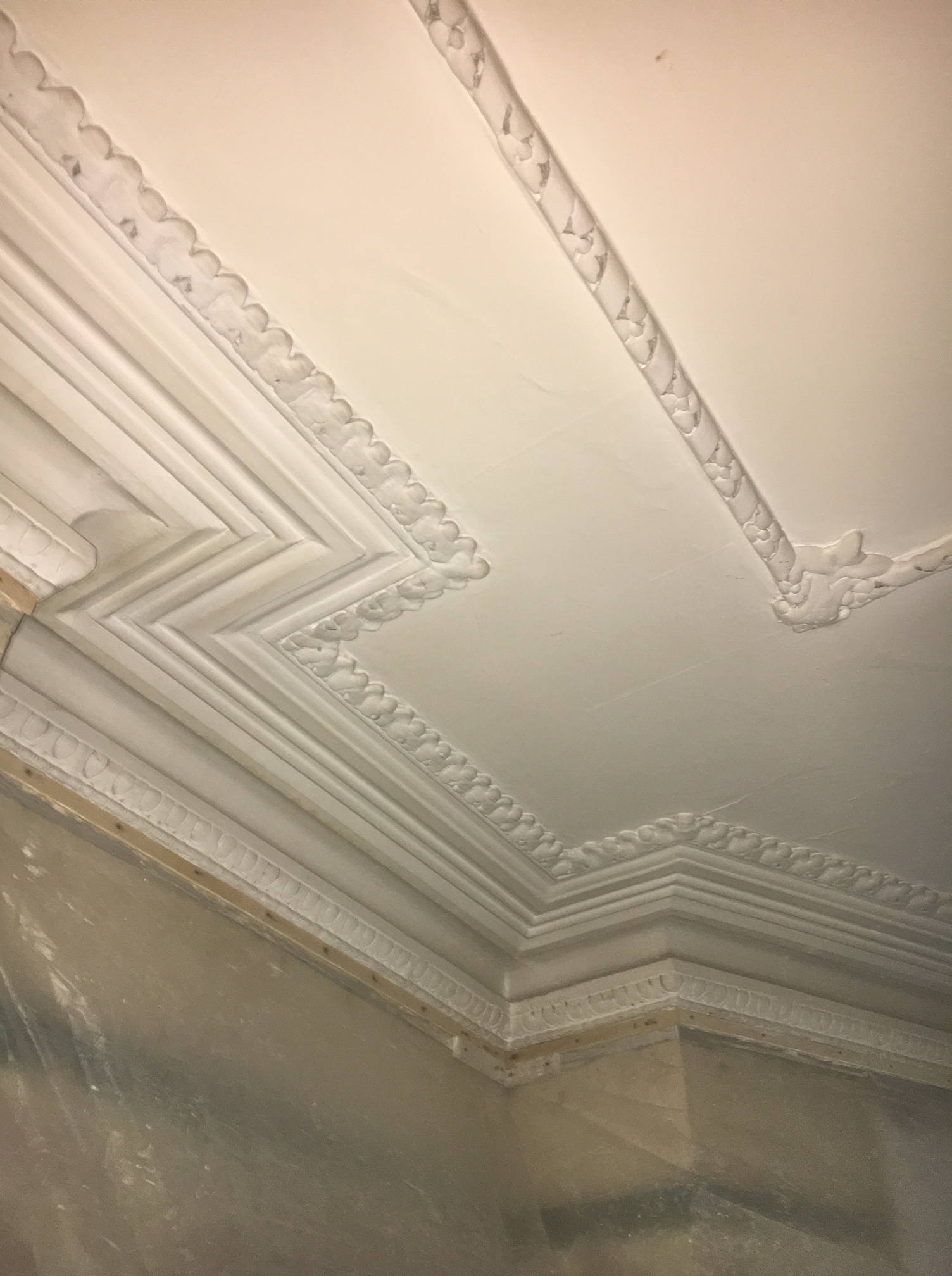 Decorative plaster cornice around a room corner with patterned ceiling borders before cleaning at Clissold Crescent.